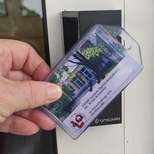 Zdjęcie przedstawia czytnik kart dostepu zainstalowany na drzwiach wejściowych z przyłożoną kartą.